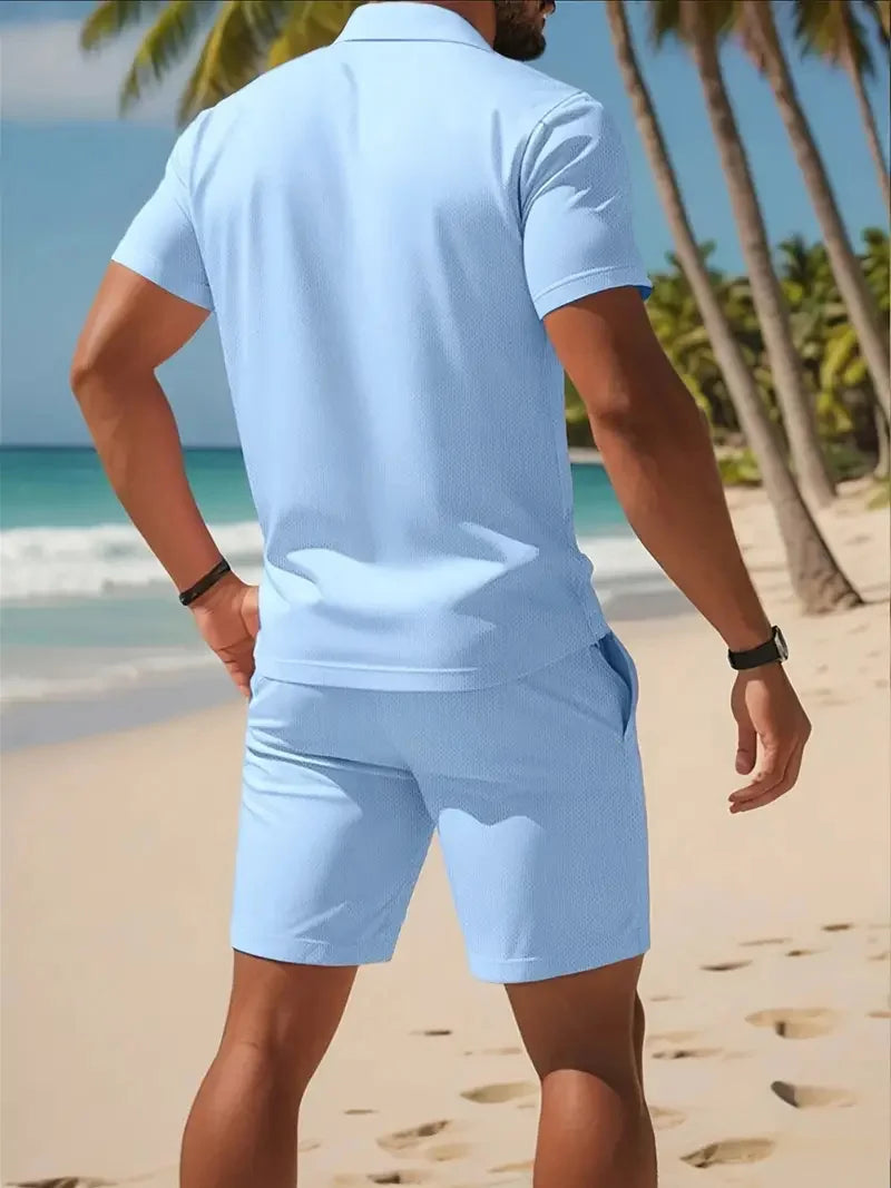 Homme portant un ensemble deux pièces homme été bleu clair sur une plage tropicale avec palmiers